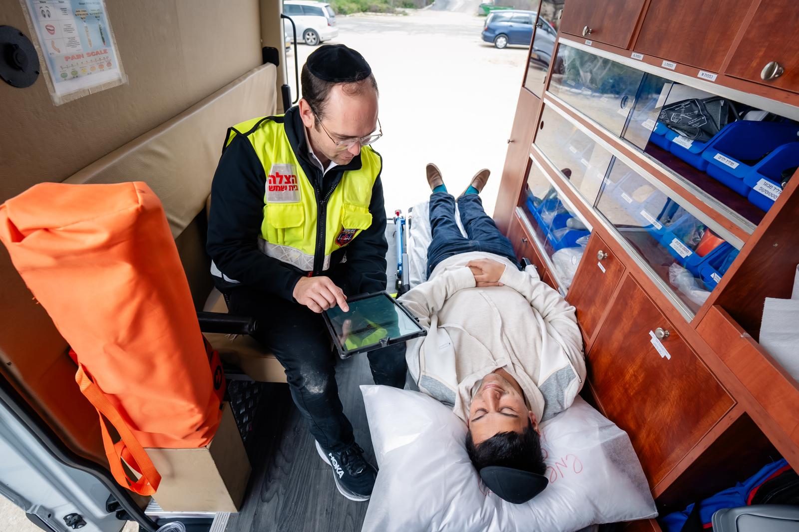 HatzBS volunteer checking notes on a tablet beside a patient